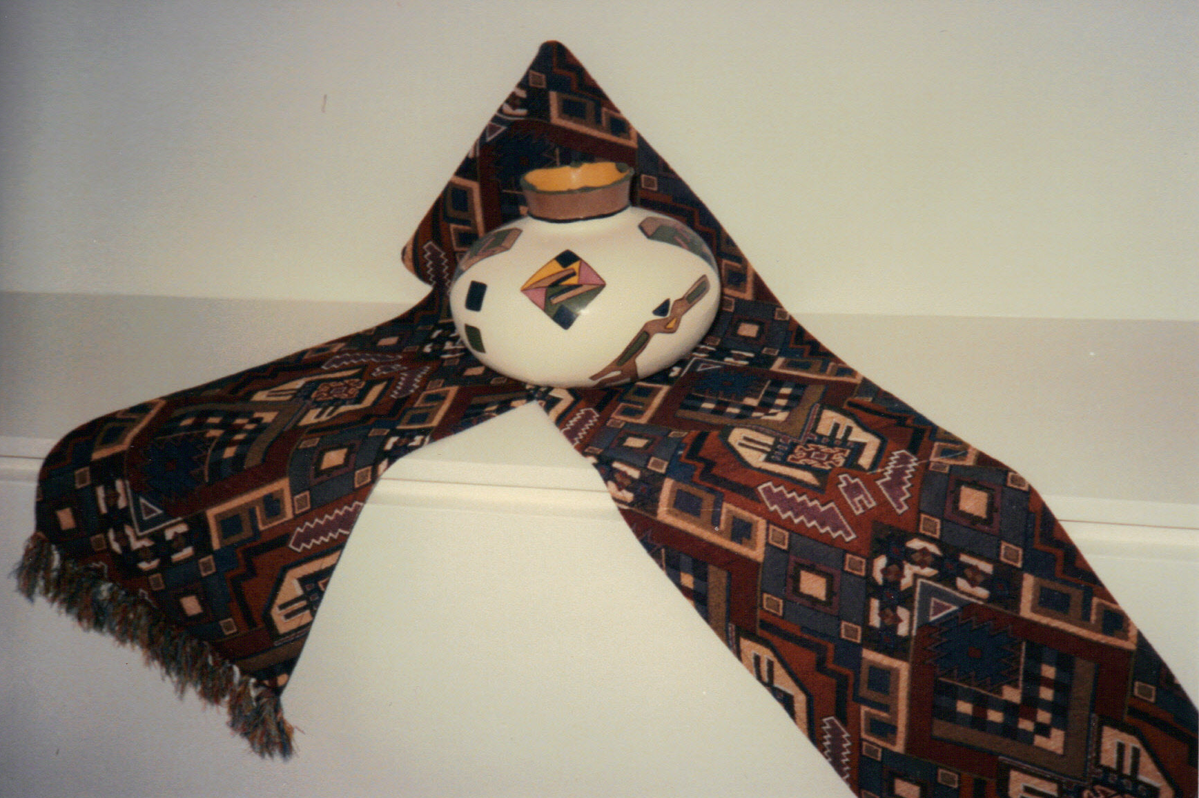A hand-painted ceramic vase sits on a richly patterned Turkish floral textile table runner draped over a shelf edge